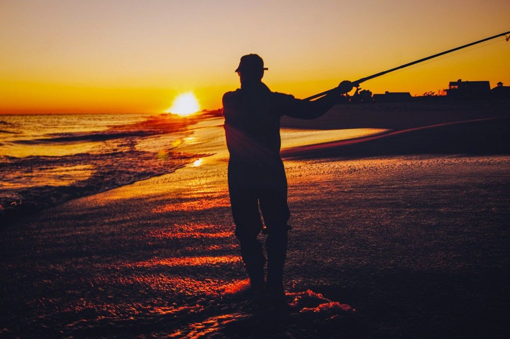 silhouette of man holding fishing rod during sunset