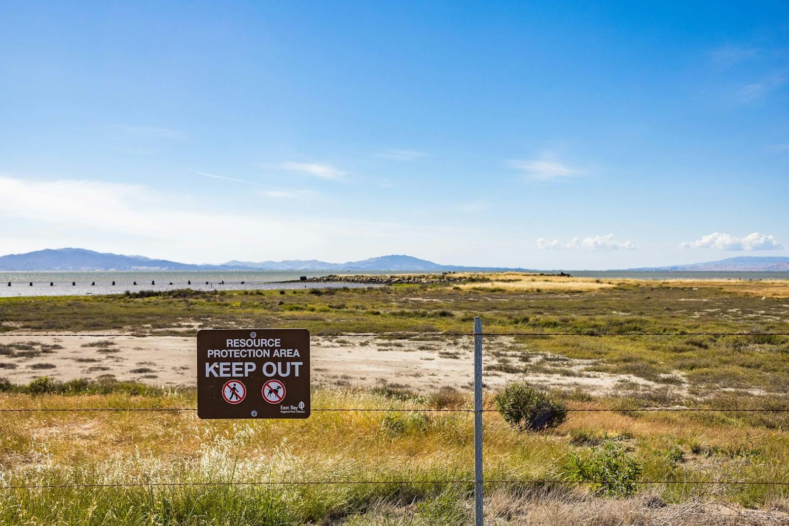 Wide view of a protected natural area with a 'Keep Out' sign and distant mountains.