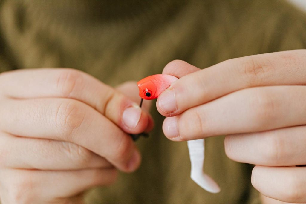 Detailed view of hands assembling a red fishing lure, highlighting fishing as a hobby.