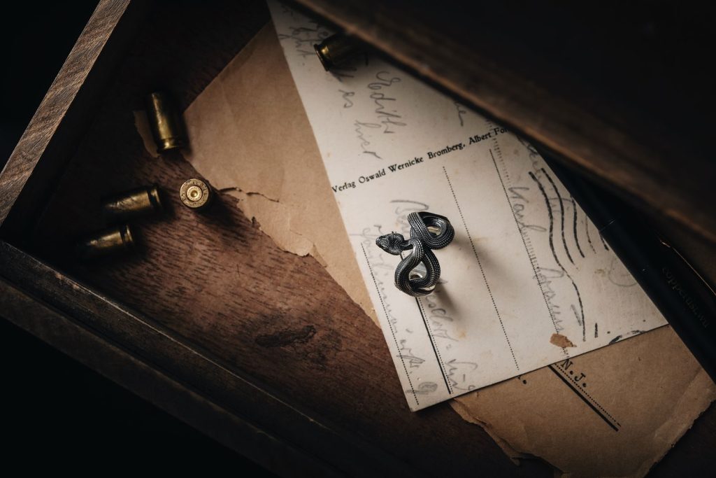 A moody still life of a vintage snake ring on an old postcard inside a wooden drawer.