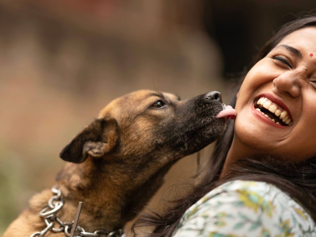 A happy woman laughs as her dog affectionately licks her in a close-up shot.