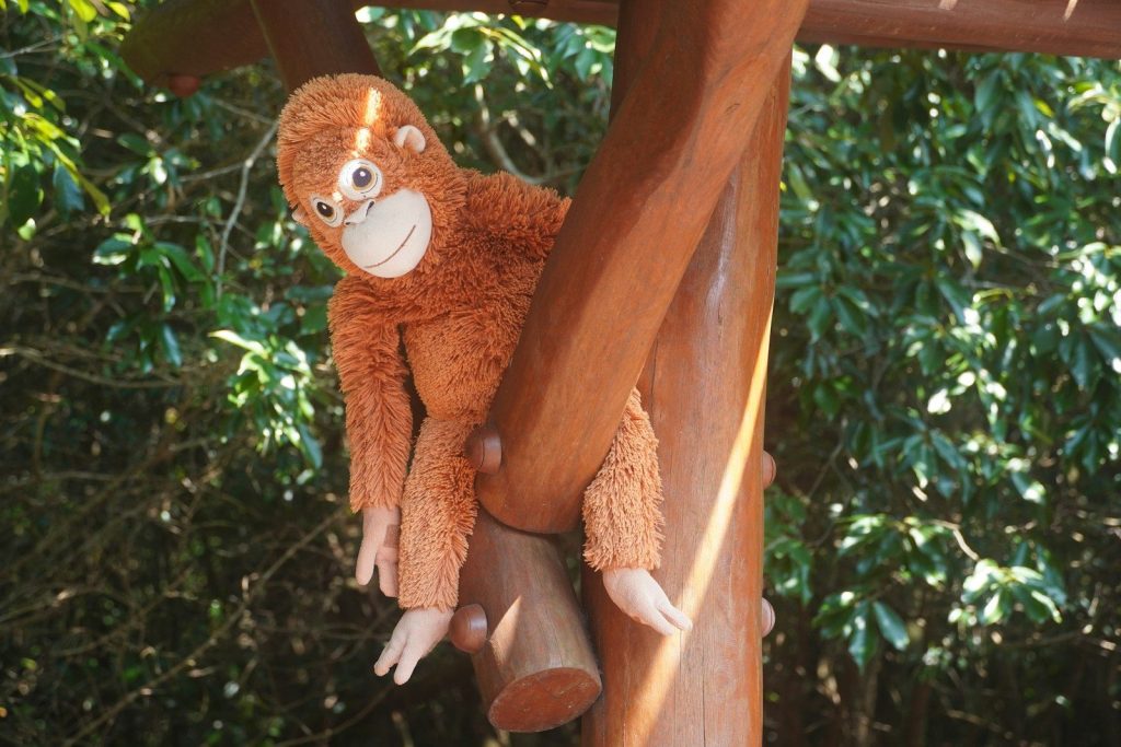 A stuffed orangutan hanging on a wooden structure.