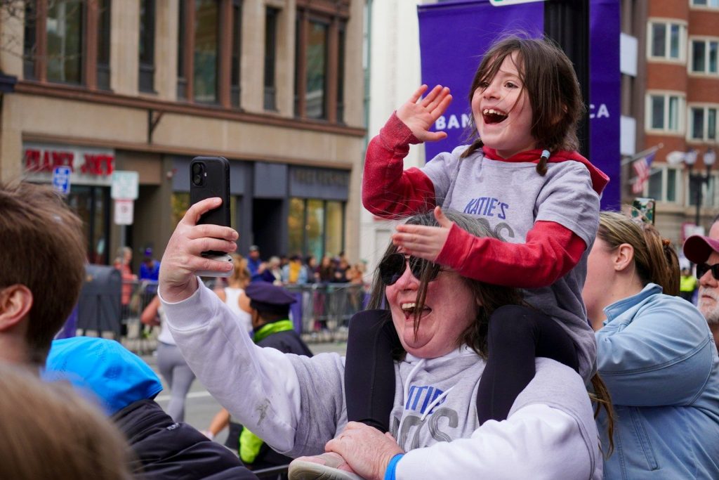 A child on shoulders taking a selfie at an event.
