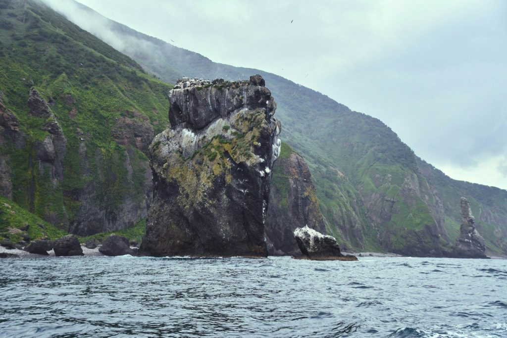 a large rock sticking out of the ocean next to a mountain