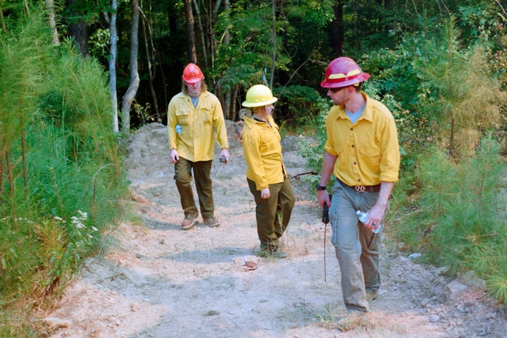 Three people in yellow shirts walk on dirt path