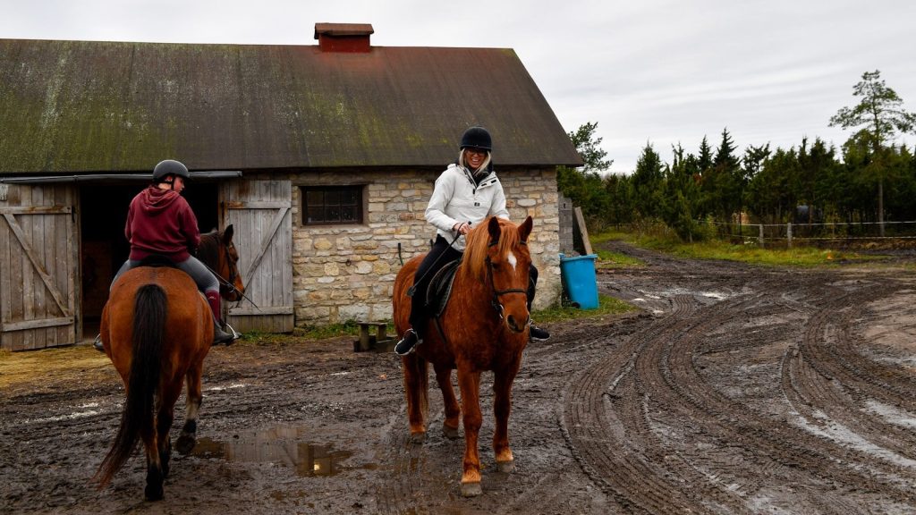 Two people riding horses near a stone building