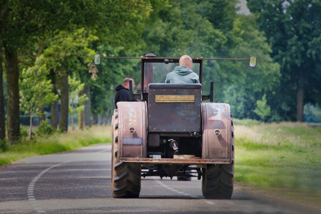 Two people are driving a tractor on a road.