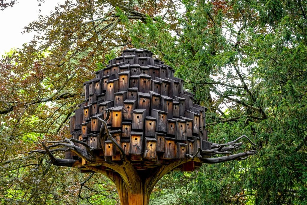 A unique wooden birdhouse installation resembling modern art amidst lush trees outdoors.