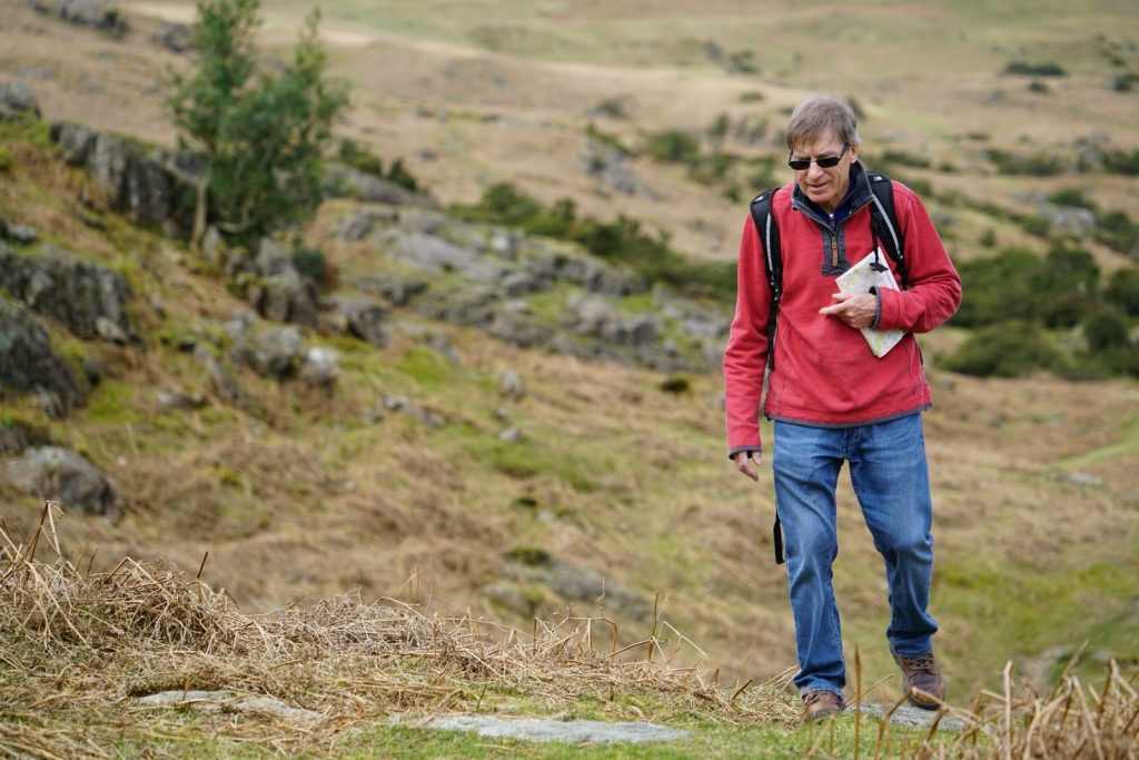 An elderly man hiking with a backpack and map in the scenic Cumbria countryside, England.