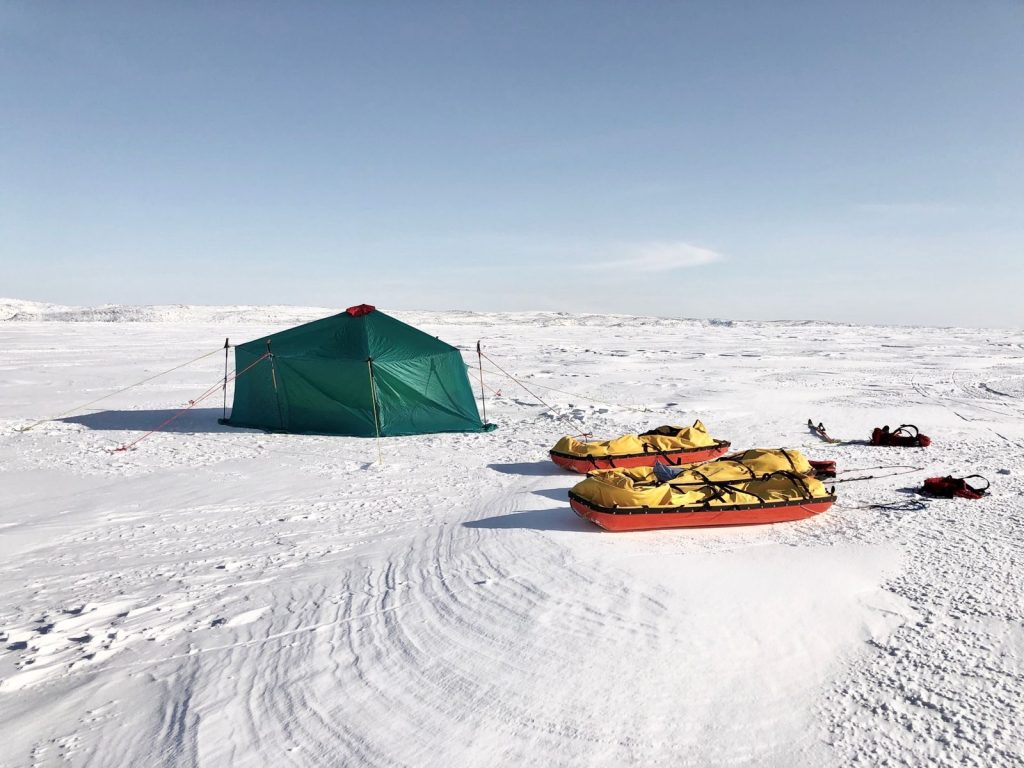 A vibrant green tent with sleds in a vast snowy landscape, ideal for winter camping adventures.