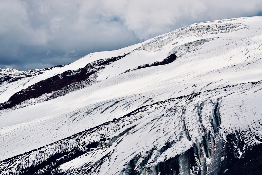 A breathtaking view of a snow-covered mountain with rugged slopes and deep crevices under a cloudy sky.