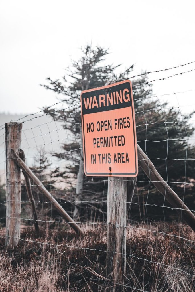 Warning sign against open fires in forested area with fence and trees, creating a clear safety message.
