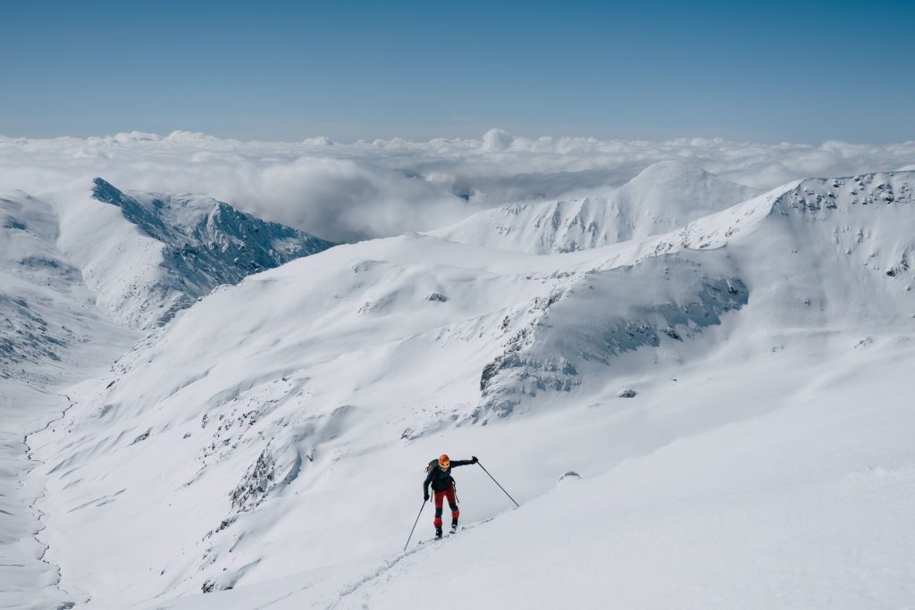 Skier climbing a snowy mountain under clear skies, showcasing winter adventure.