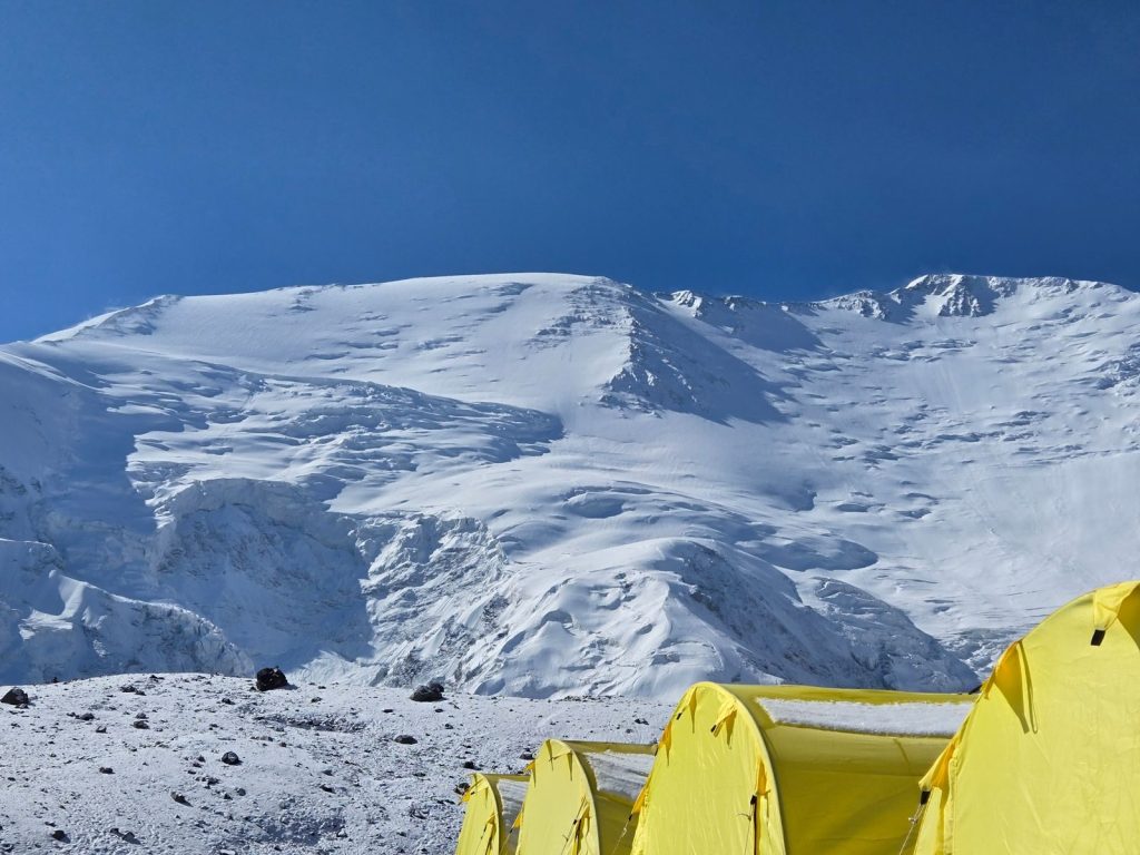 Bright yellow tents on a snowy mountain under clear blue skies, ideal for adventure seekers.