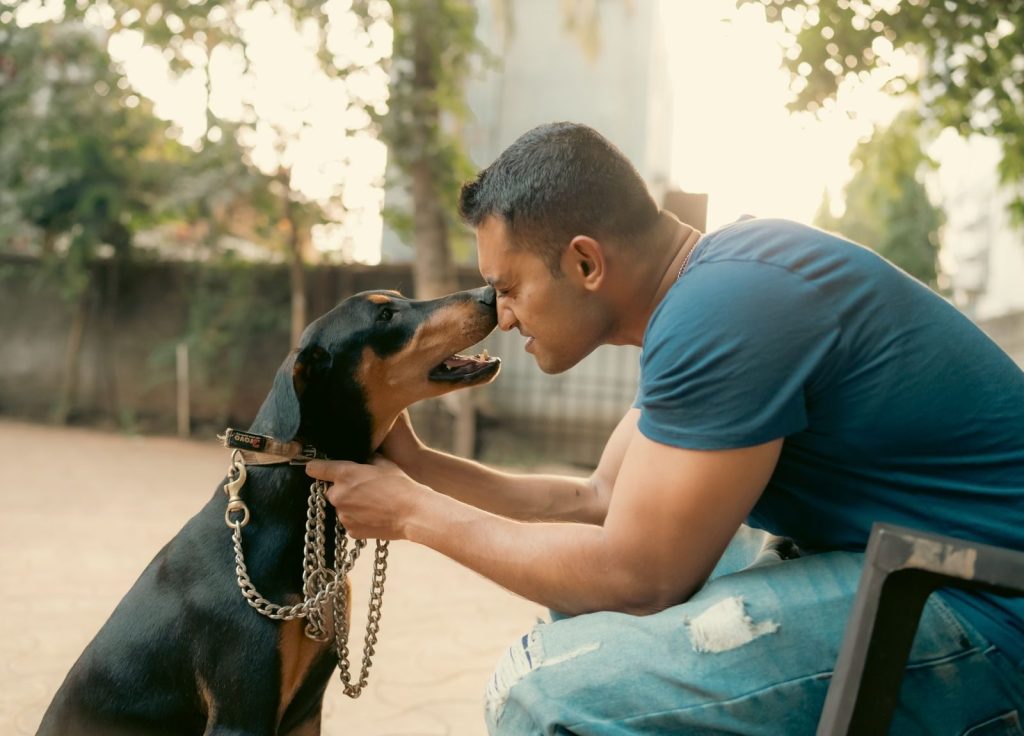 A man and a Doberman interact warmly outdoors, showcasing companionship.