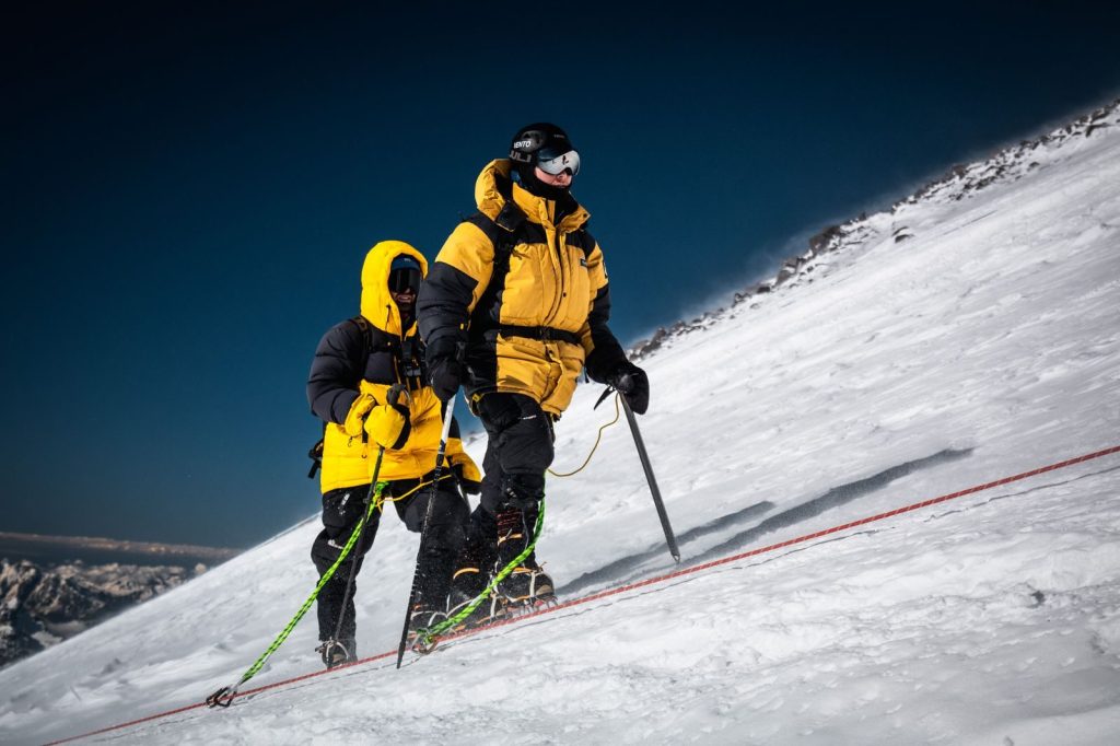 Two climbers in yellow jackets navigate a snowy mountain slope in Russia, showcasing winter adventure.