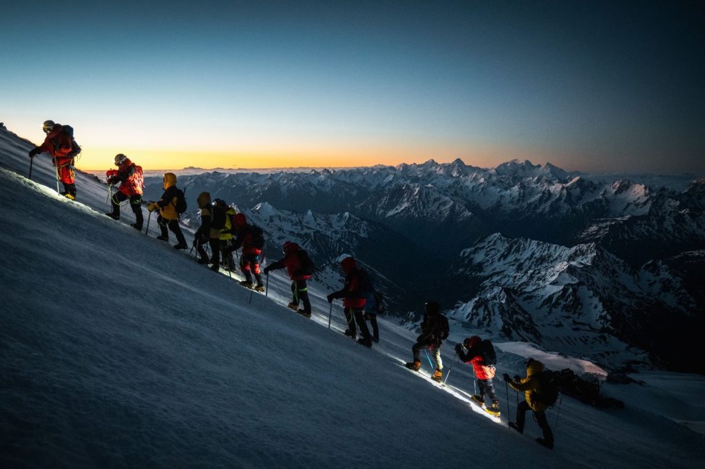 A group of climbers ascend Mount Elbrus at dawn, showcasing teamwork and adventure in the snowy Caucasus Mountains.
