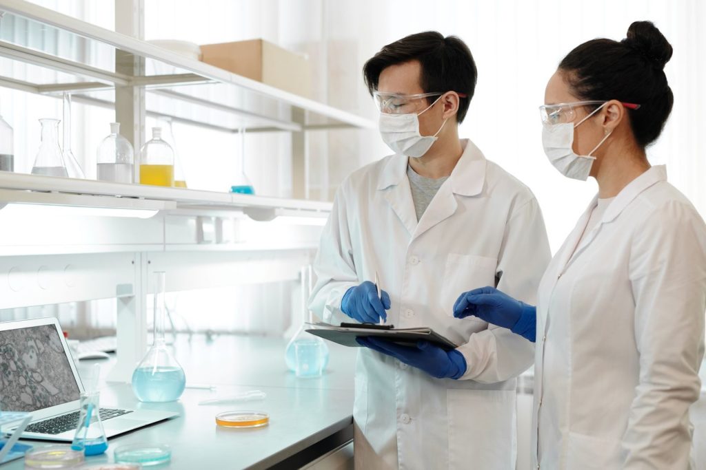 Researchers in laboratory wearing masks, gloves, and goggles working on scientific experiments.