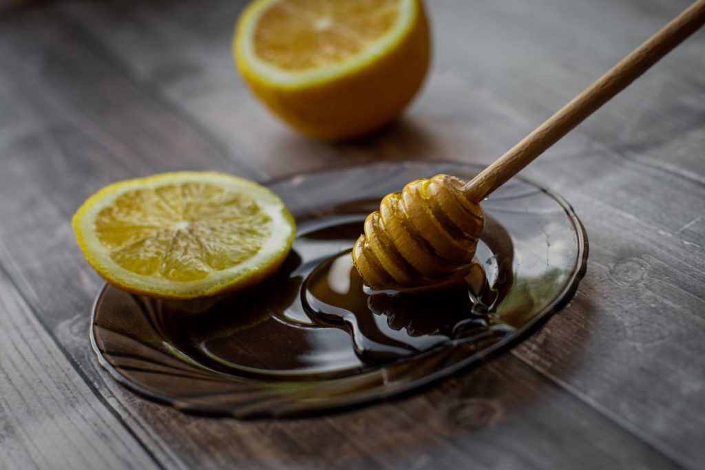 Honey dipper placed on saucer with lemon slice and sweet honey on wooden table