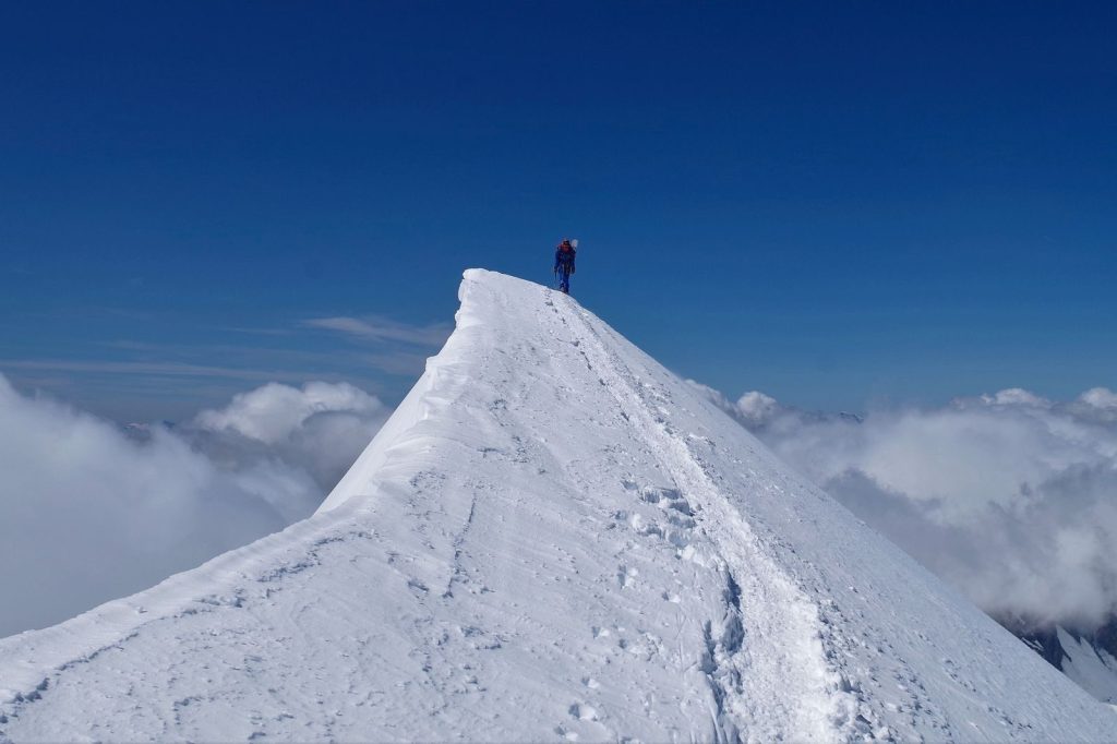 Explorer stands atop a snowy summit above the clouds, capturing a breathtaking scene.