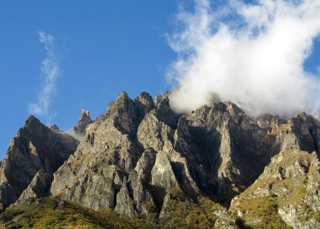 Jagged mountain peaks shrouded in clouds under blue sky