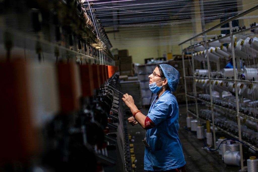 A factory worker checks threads on a large machine.